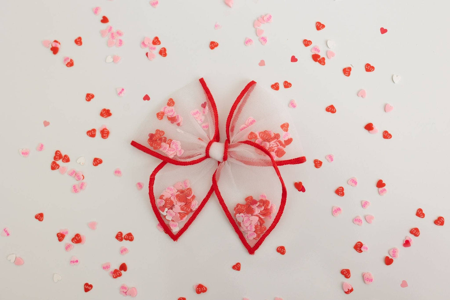 A small red mesh shaker bow filled with heart confetti, perfect for Valentine's gifts.
