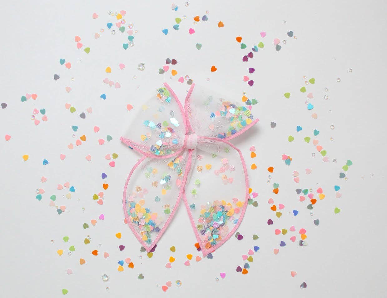 Large pink-edged bow with pastel heart confetti inside, surrounded by a sprinkle explosion.