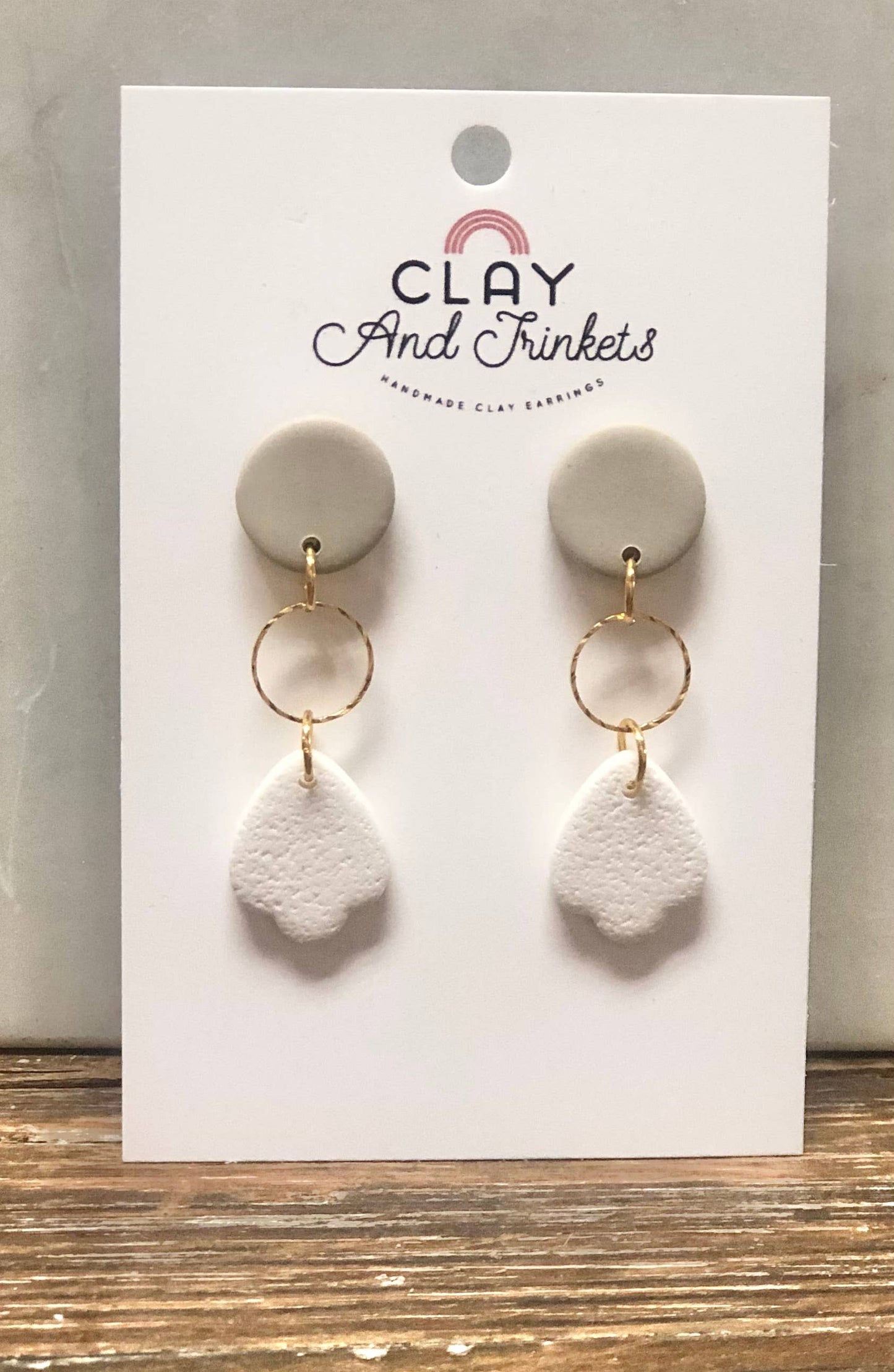 White petal-shaped clay earrings with gold ring accents on a display card