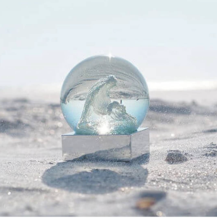 Glass snow globe with ocean wave design, featuring a clear glass sphere on a white base.