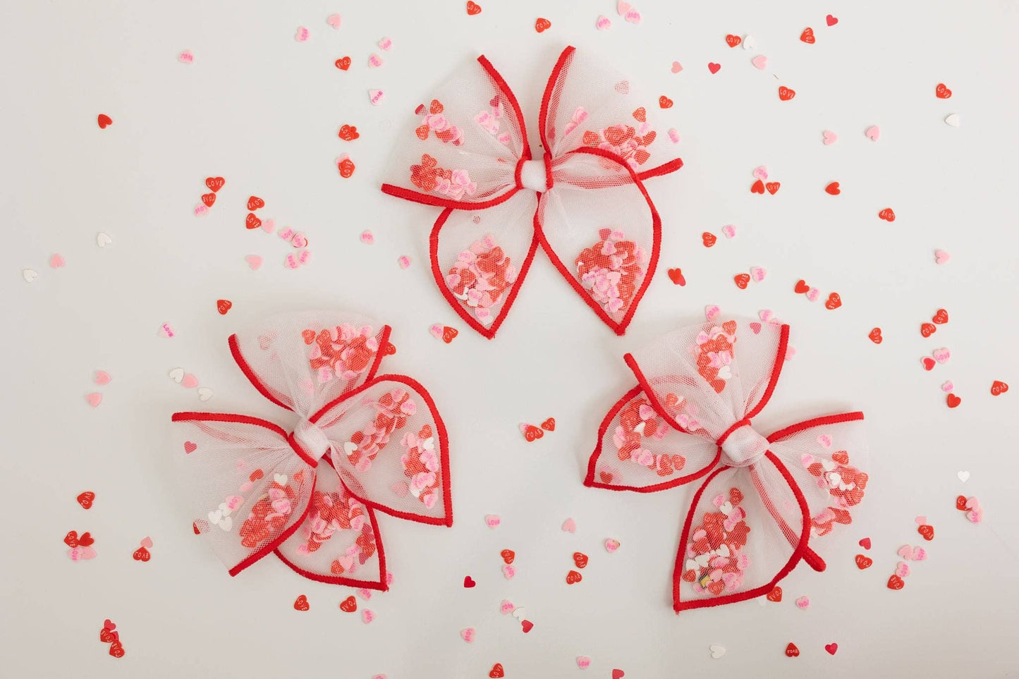A small white mesh bow with red trim and heart confetti, perfect for Valentine's gifts.