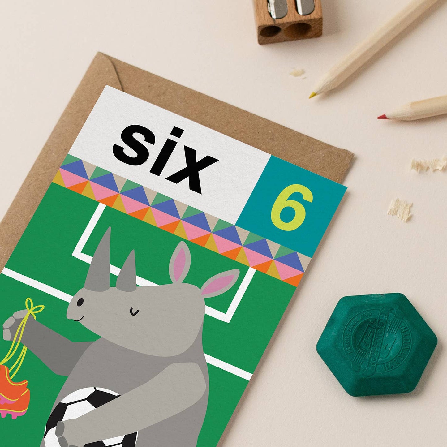 A colorful birthday card for age 6 featuring a rhino playing football on a green field with a rainbow border.