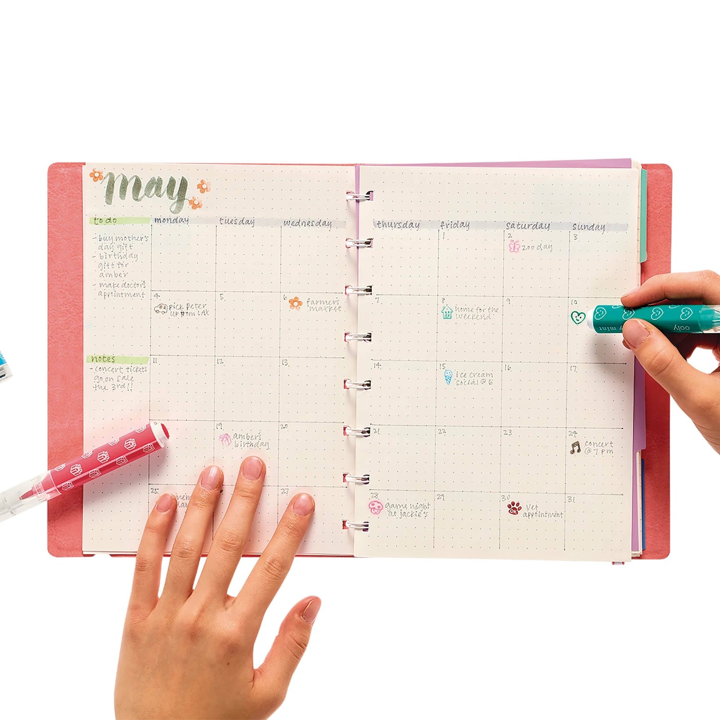 A pink planner with a May calendar page, featuring handwritten notes and colorful stamps.