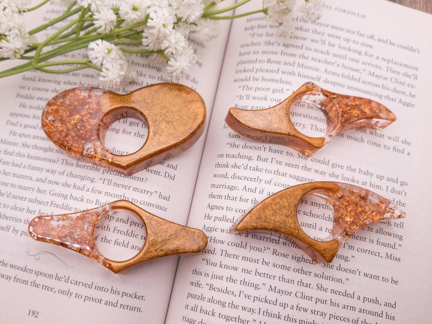 Handcrafted rose gold and copper book page holders resting on an open book with white flowers nearby.