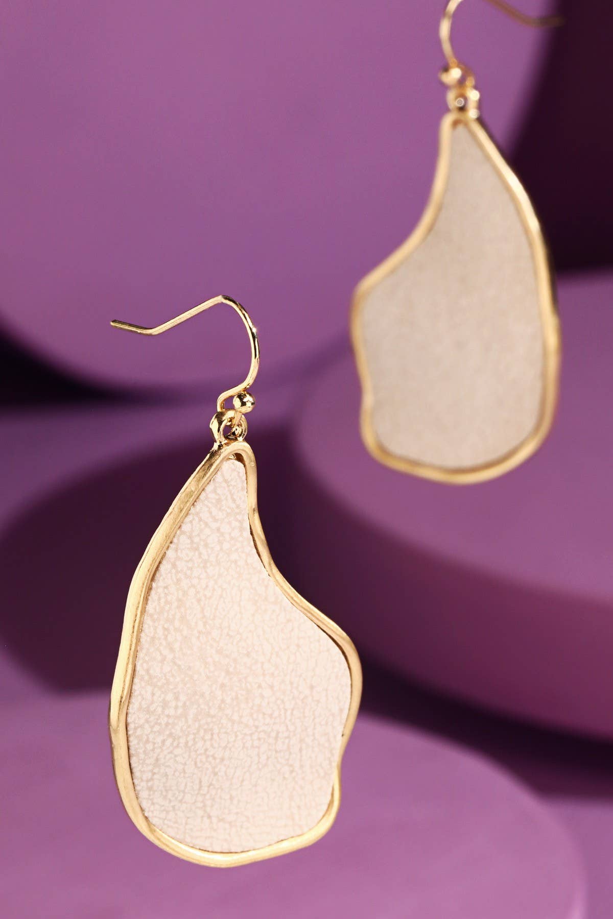 Organic shaped ivory dangle earrings with gold trim on purple background