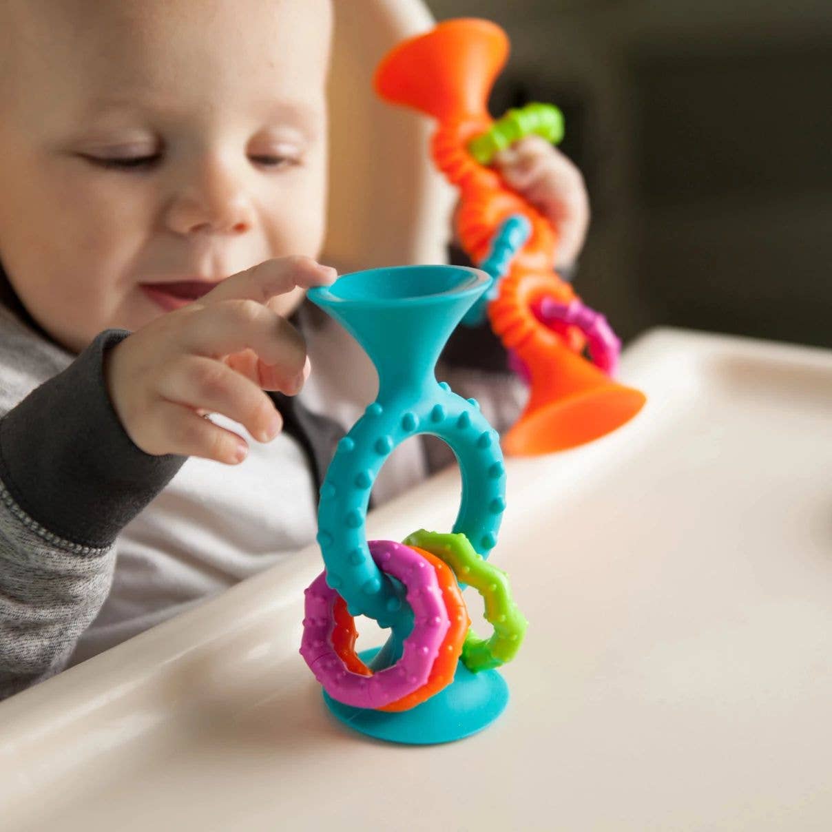 Toddler playing with blue and orange suction toys with rattling rings and tactile bumps.