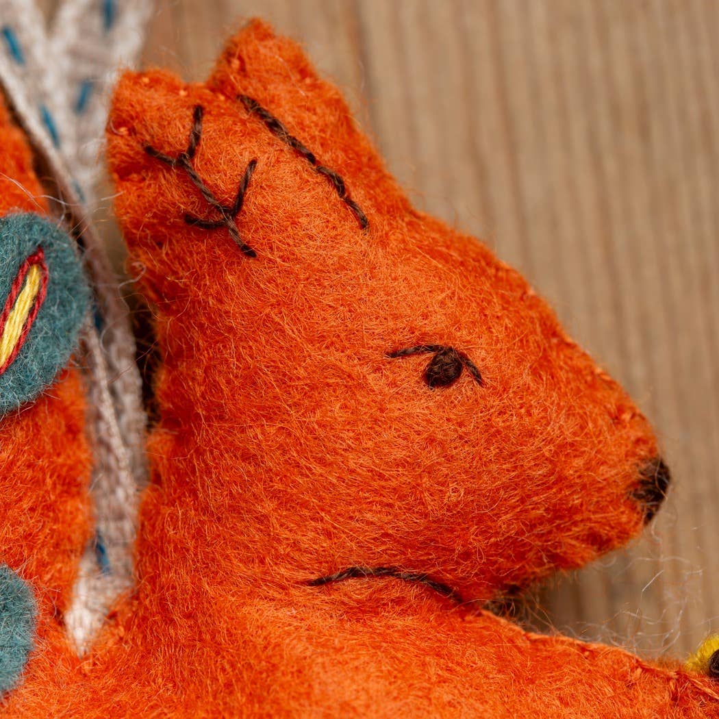 Handmade felt squirrel with orange fur, stitched details, and a colorful tail, perfect for crafting.