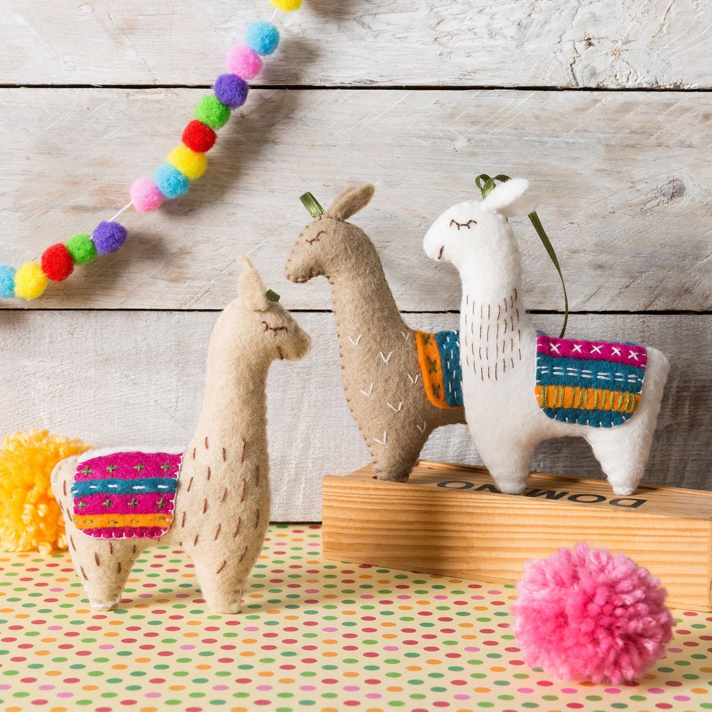 Colorful handmade felt llamas with embroidered rugs on a polka dot background.
