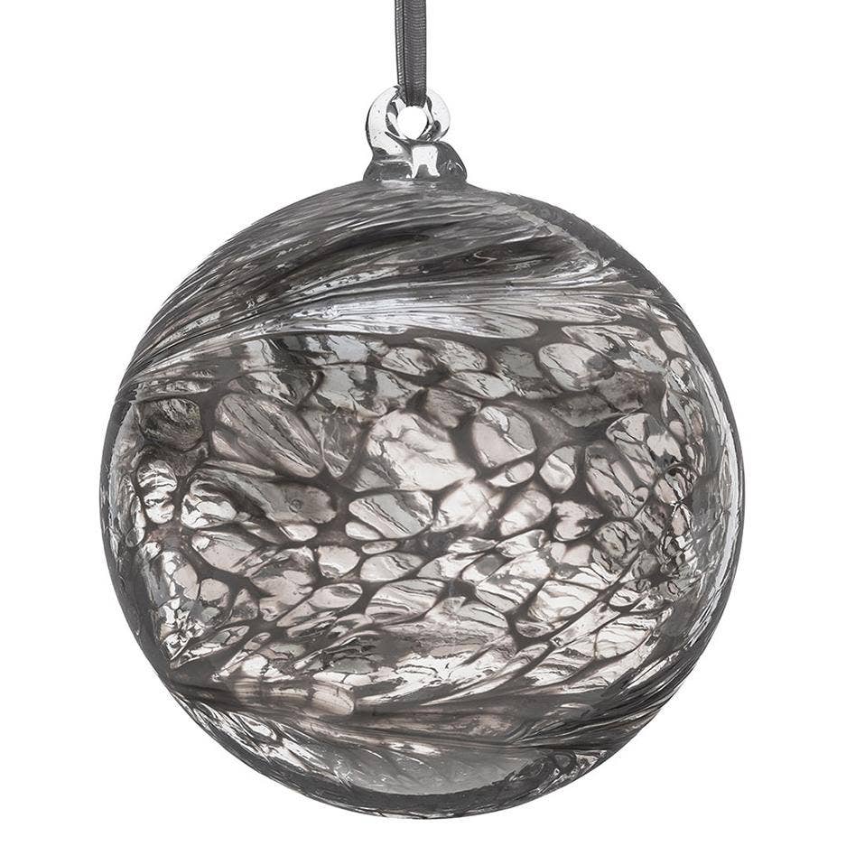 Glass ornament with a translucent pastel silver tree inside, surrounded by faint lilac, yellow, and pink petals, hanging by a yellow ribbon.