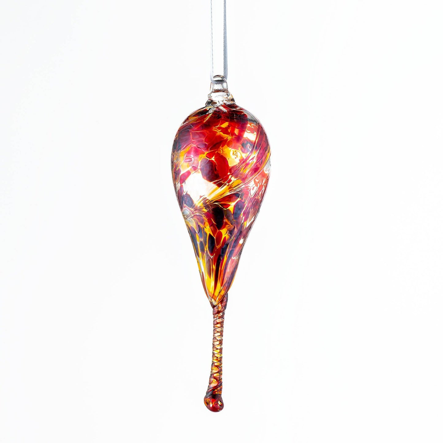 Teardrop-shaped glass ornament in warm red, orange, and gold tones with a twisted clear tail, suspended from a silver string.