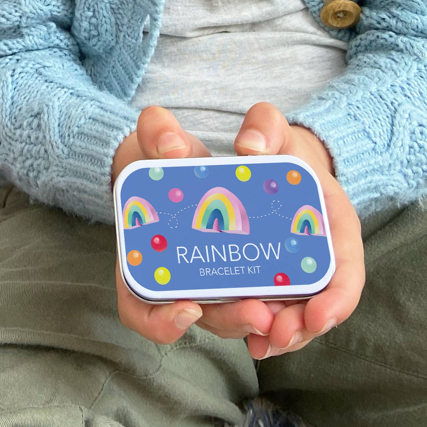 Eco-friendly rainbow bracelet kit in a blue tin with colorful rainbows and bubbles design.
