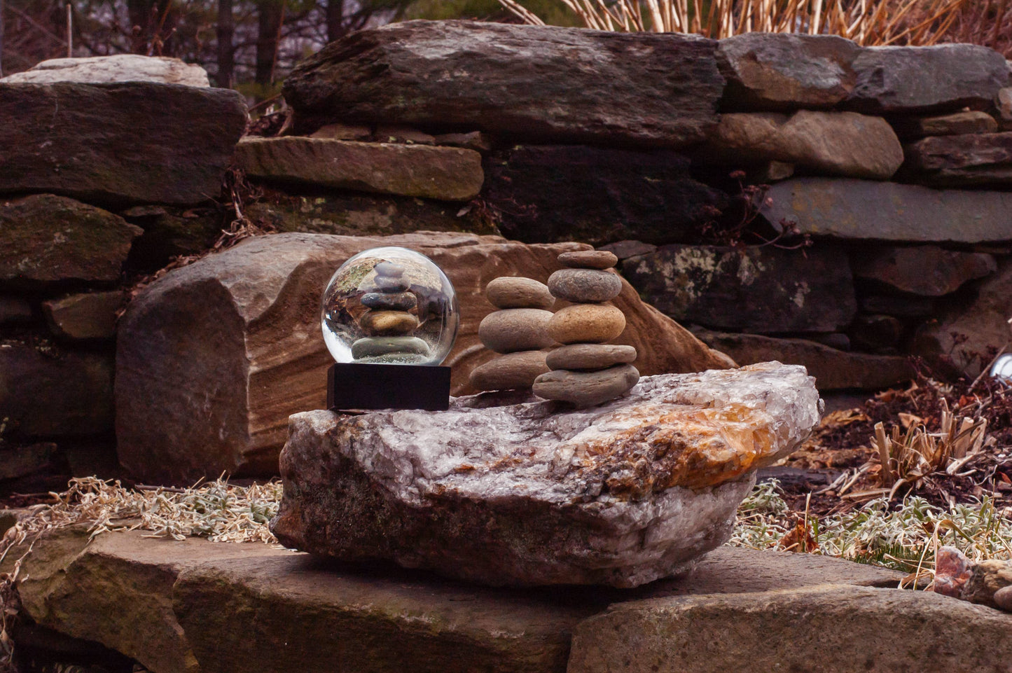 A Cairn Snow Globe with stacked stones on a black base, featuring unique craftsmanship and natural stones.