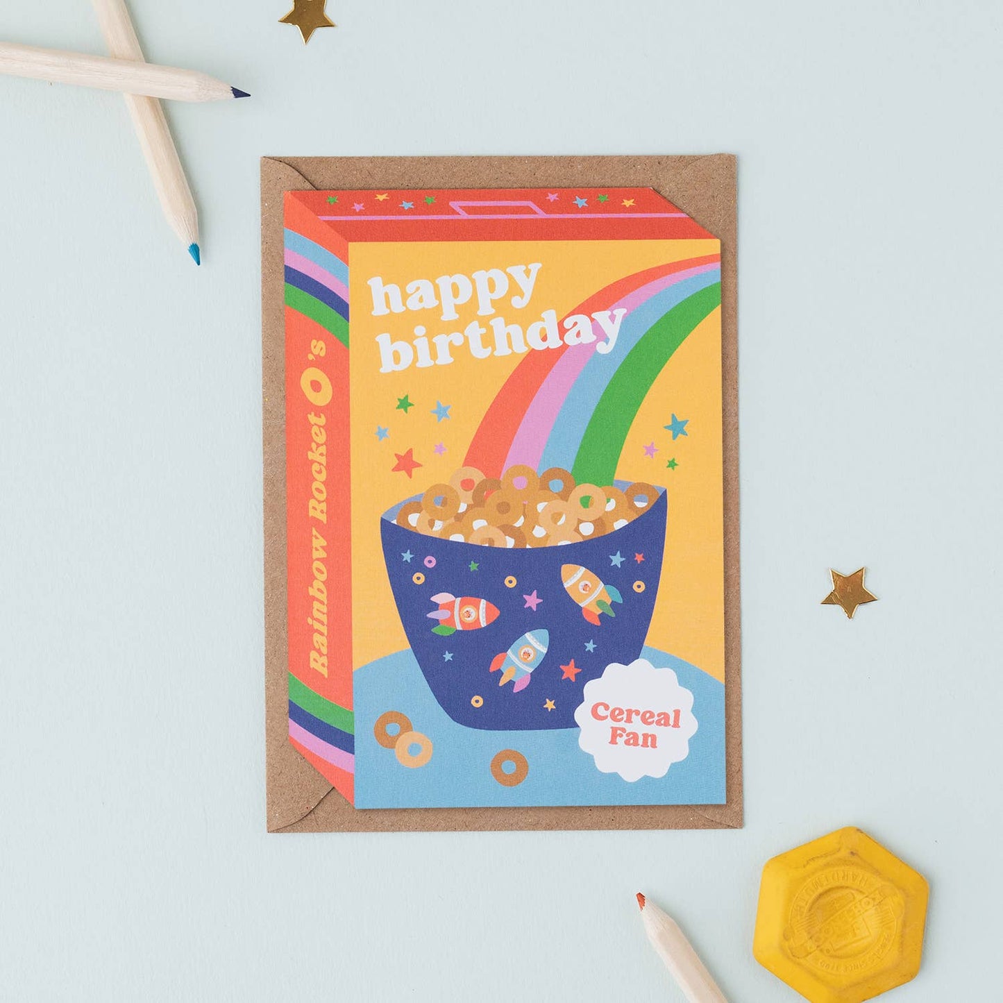 A colorful birthday card featuring a cereal box with a rainbow, stars, and a bowl of cereal rings.