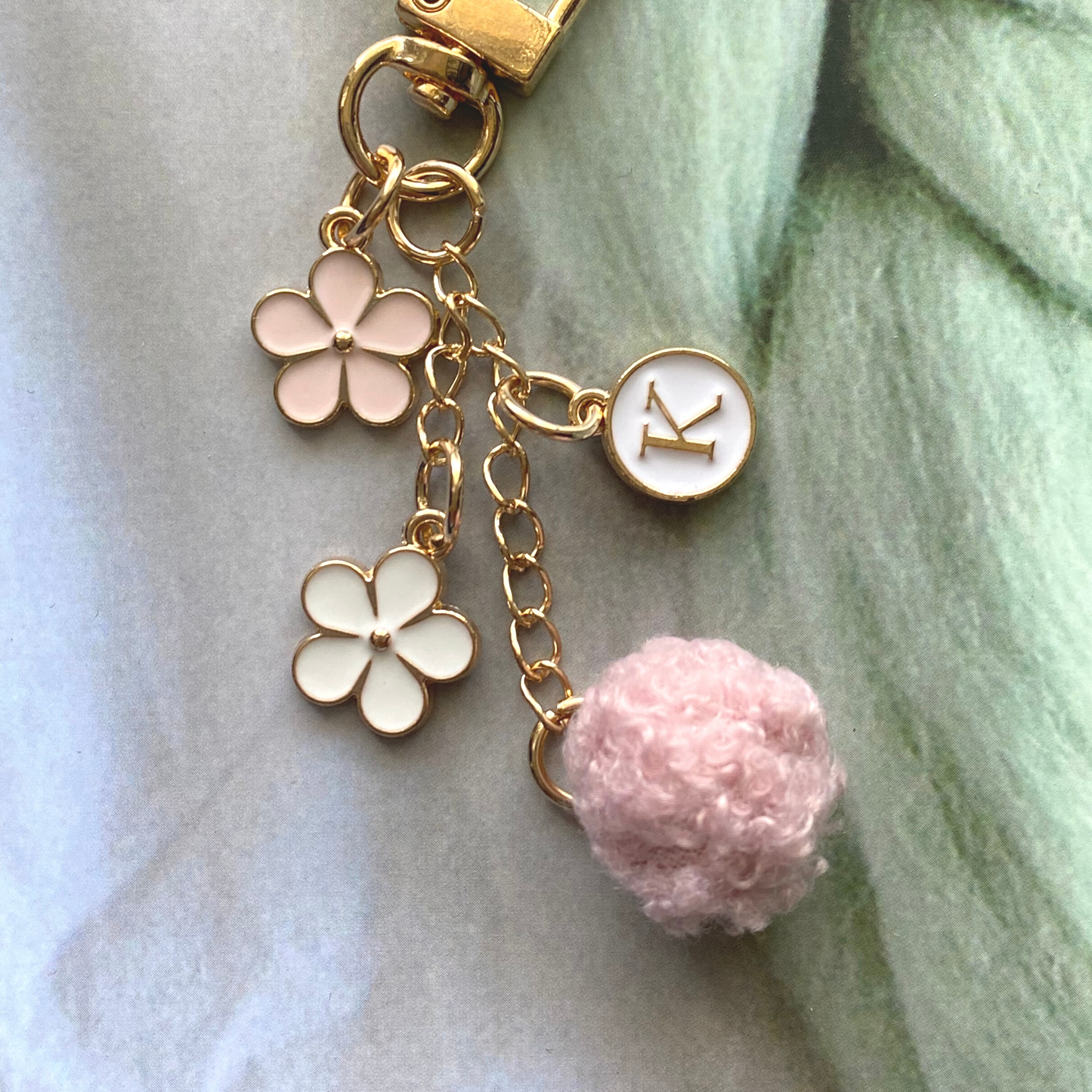 Floral initial keychain with pink and white flower charms, a gold initial pendant, and a soft pink pom charm.