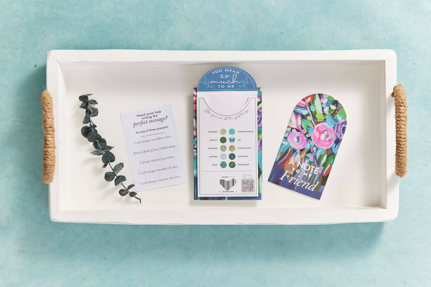 A white tray with a floral card, a message prompt, and a leafy branch.