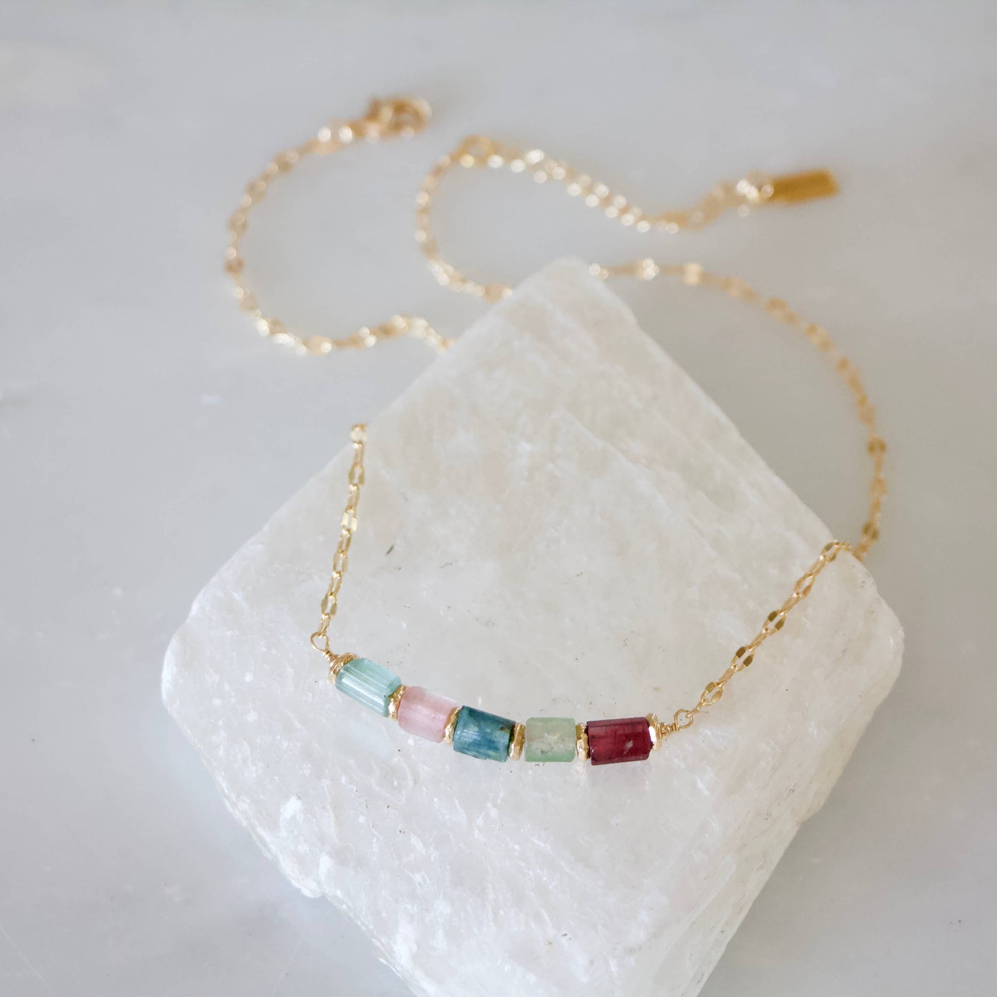 Gold collar necklace with multicolored tourmaline nuggets on a white crystal background