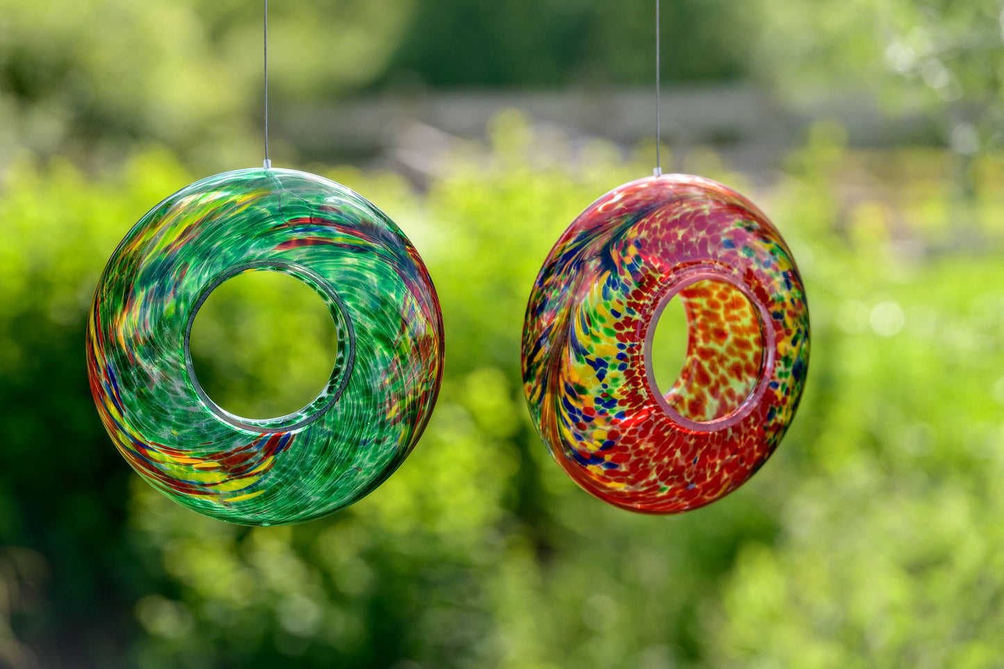 Red hand-blown glass bird feeder with vibrant, multicolored swirls and a circular design.