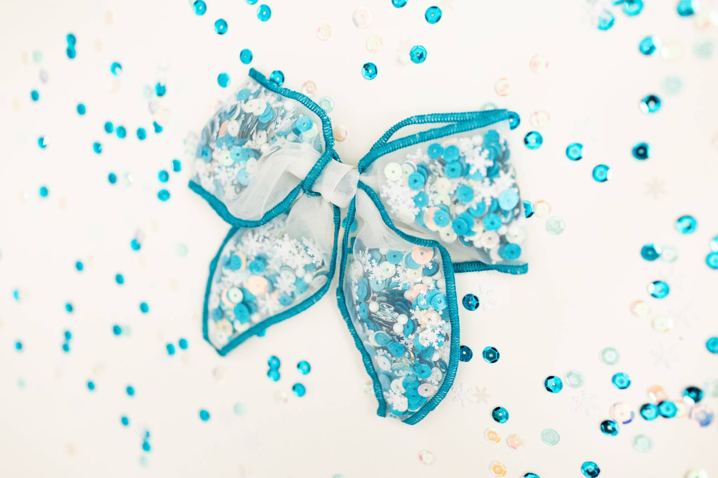 Large blue-edged mesh bow filled with white and aqua sequins and snowflake confetti for a wintery effect.