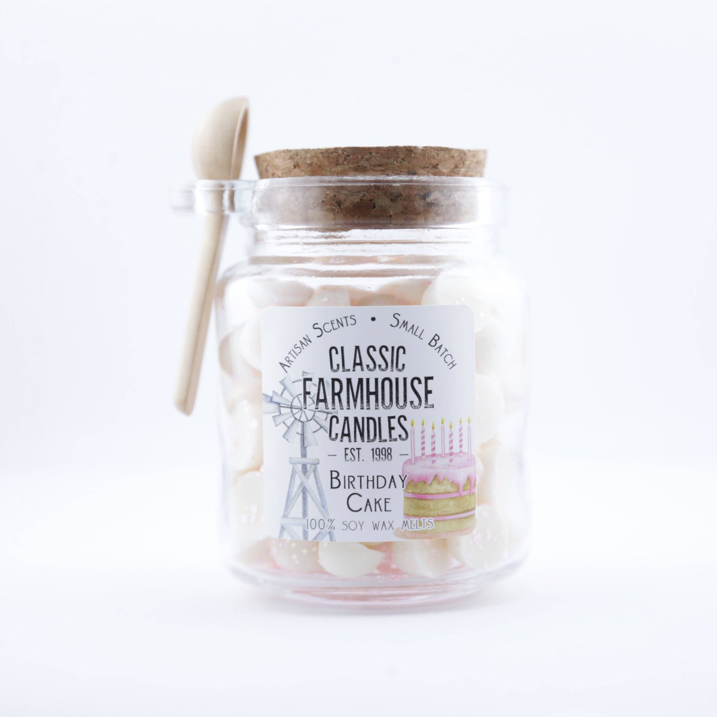 Glass jar filled with pink-and-white wax melts labeled "Birthday Cake", topped with a cork and a mini spoon on the side.
