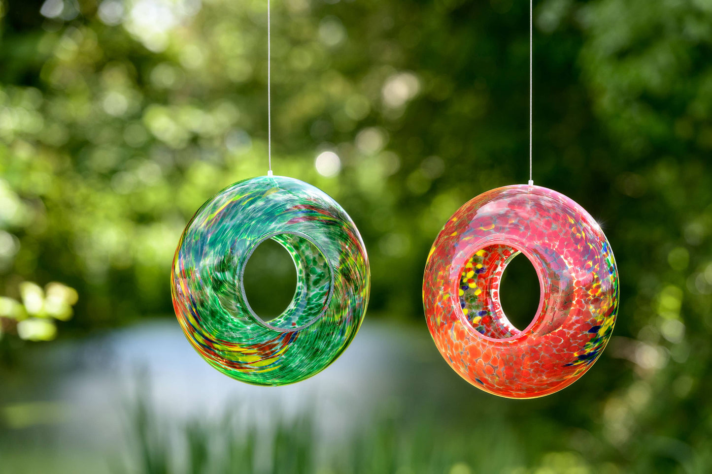 Red hand-blown glass hanging bird feeder with a vibrant, circular design and speckled pattern.