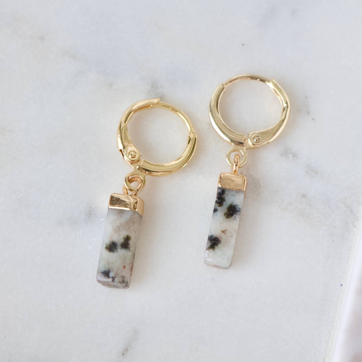 Gold huggie earrings with rectangular white turquoise stones featuring black speckles.