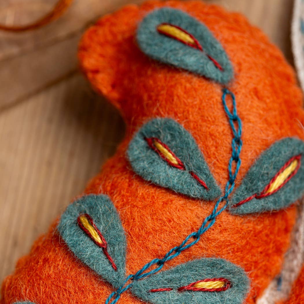 Bright orange felt squirrel with blue and yellow embroidered details, perfect for crafting.
