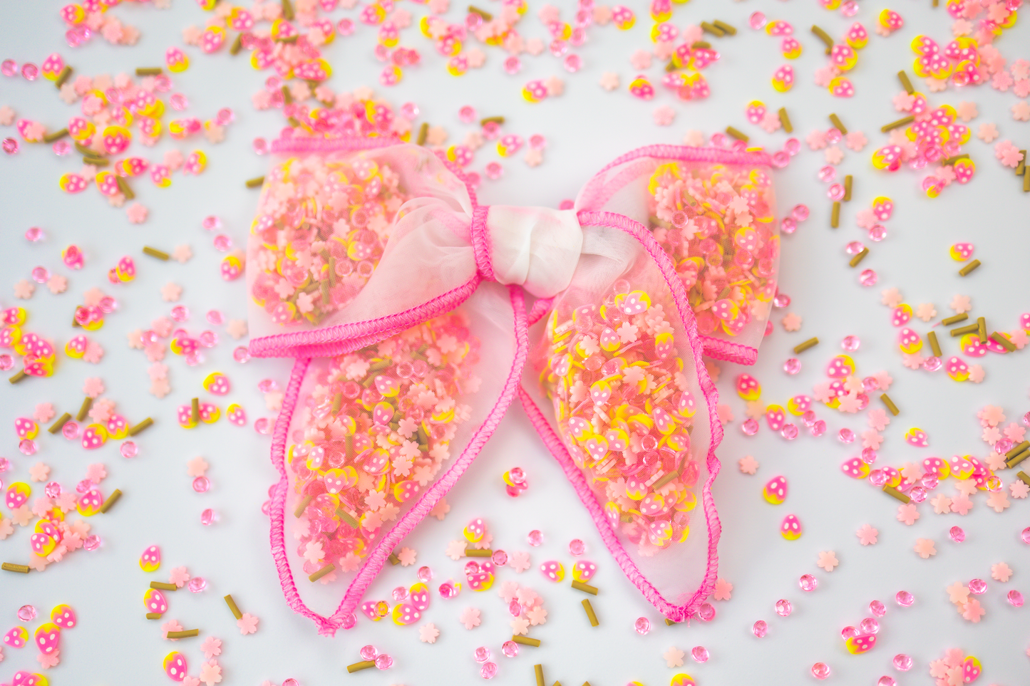 Transparent pink bow with strawberry-shaped confetti inside, paired with heart-shaped sprinkles.