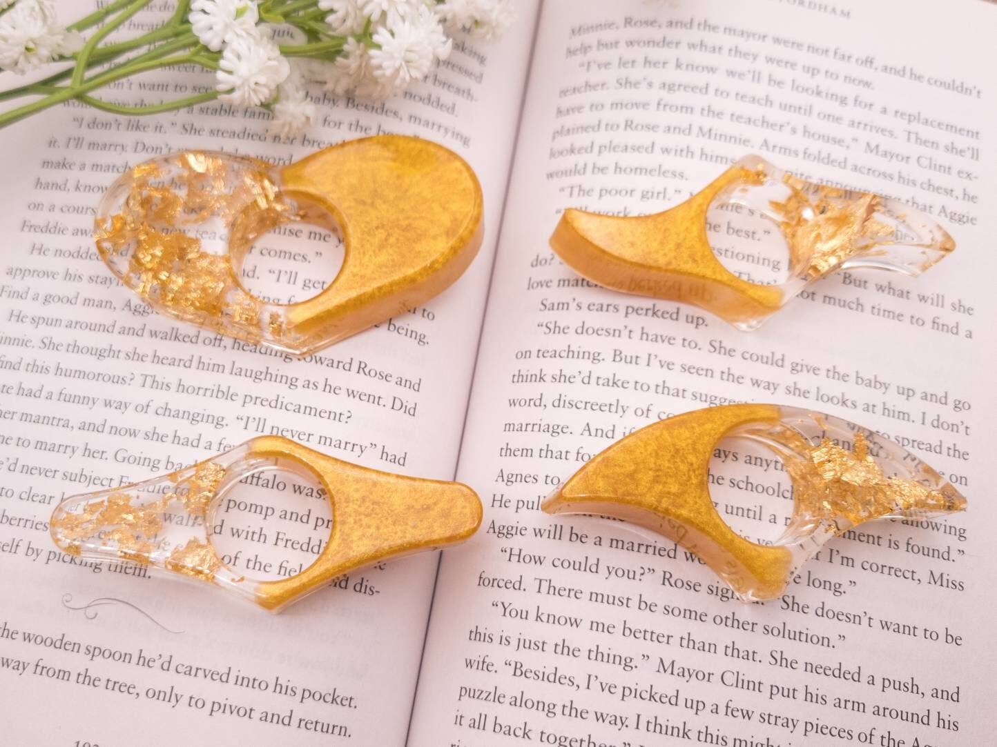 Gold and clear resin book page holders on an open book with white flowers