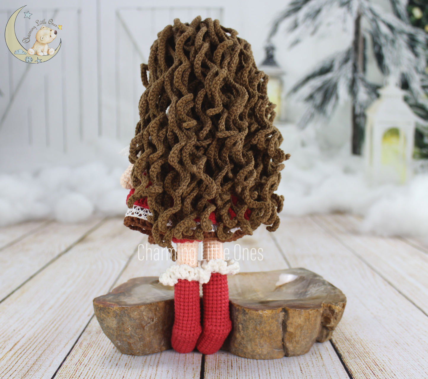 A handmade crochet doll with curly brown hair, red outfit, and wooden stand.