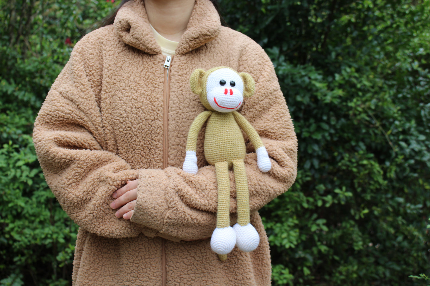 A handmade crochet monkey toy with a yellow body, white face and feet, and red nose.