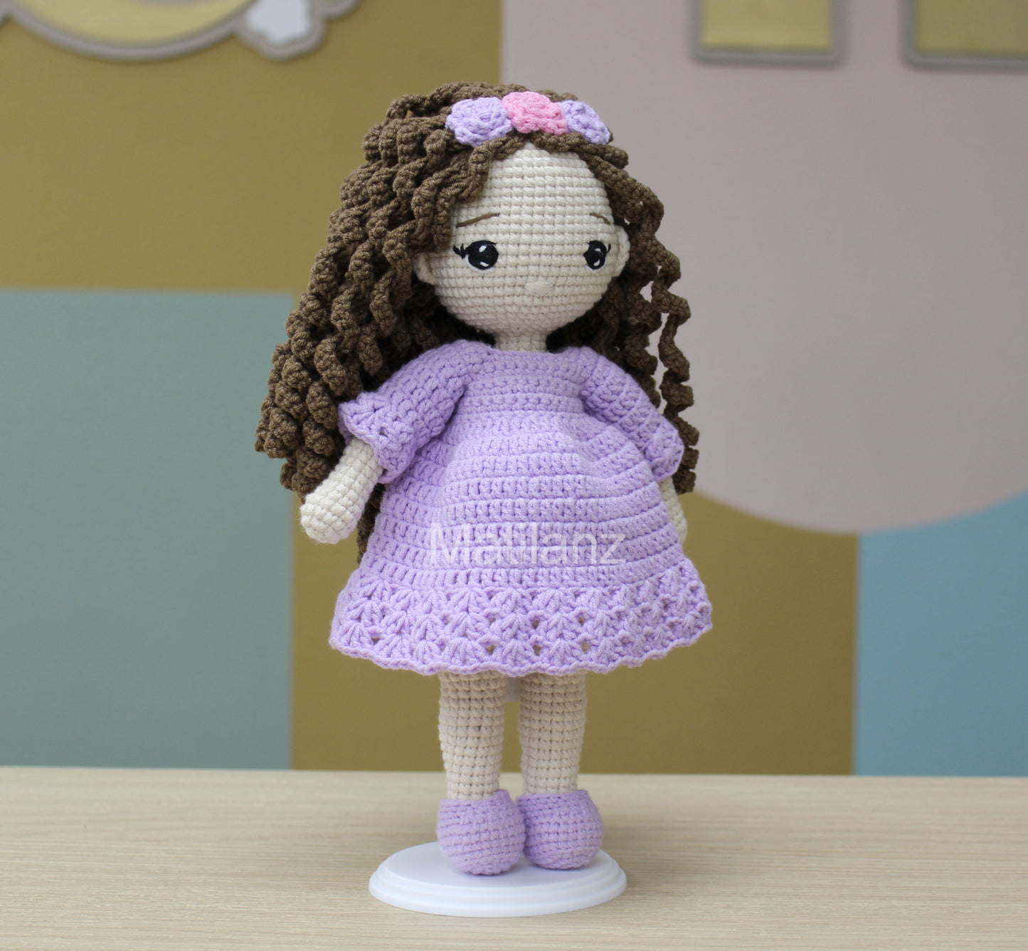 Crochet doll with purple dress, curly brown hair, and matching shoes, adorned with a floral headband.