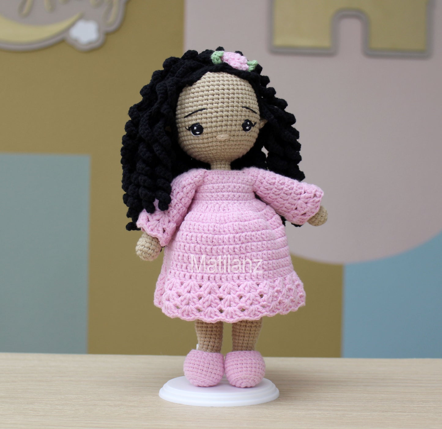 Crochet doll with black curly hair, wearing a pink dress and matching shoes, handmade with intricate details.