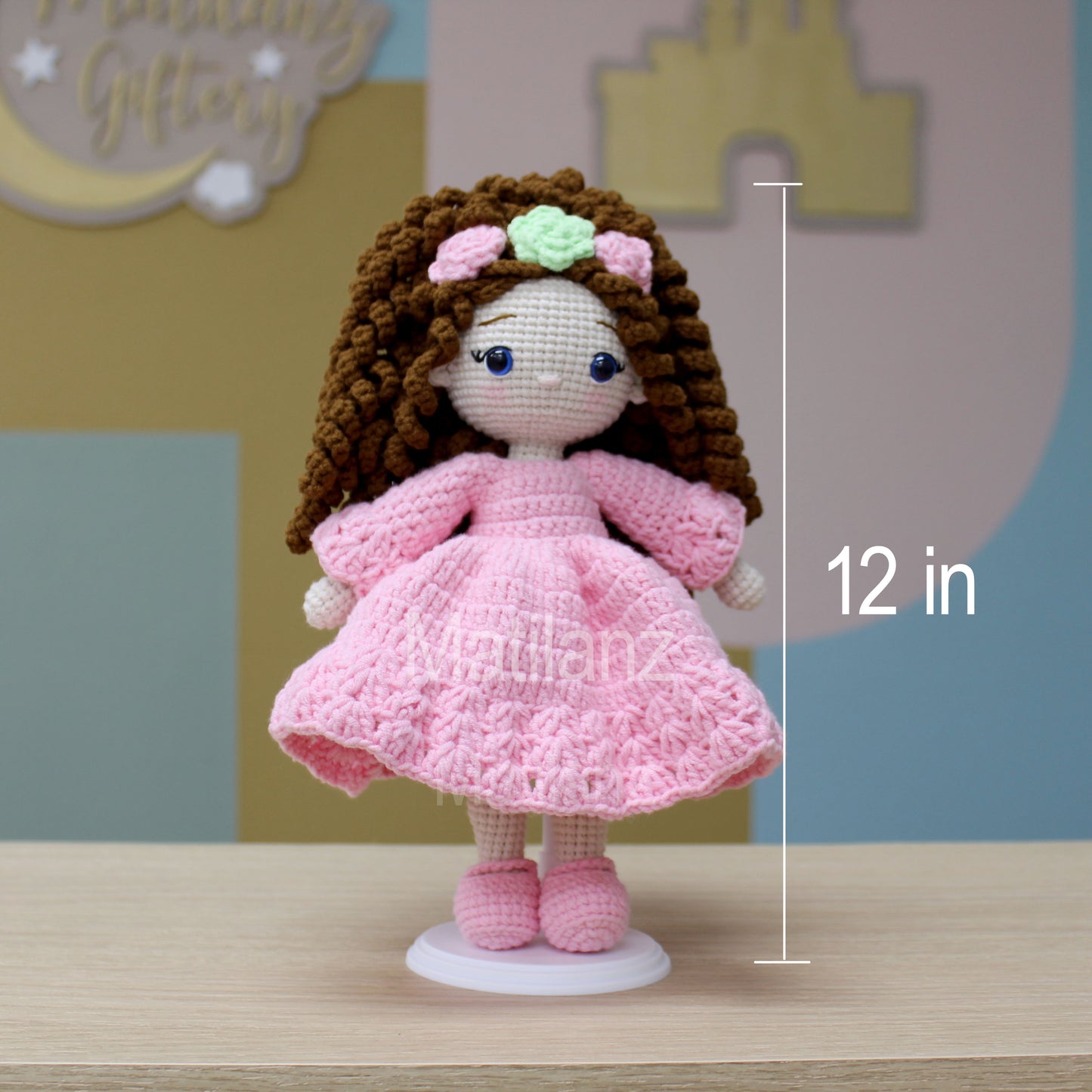 A 12-inch handmade crochet doll with curly brown hair, pink dress, and flower headband.