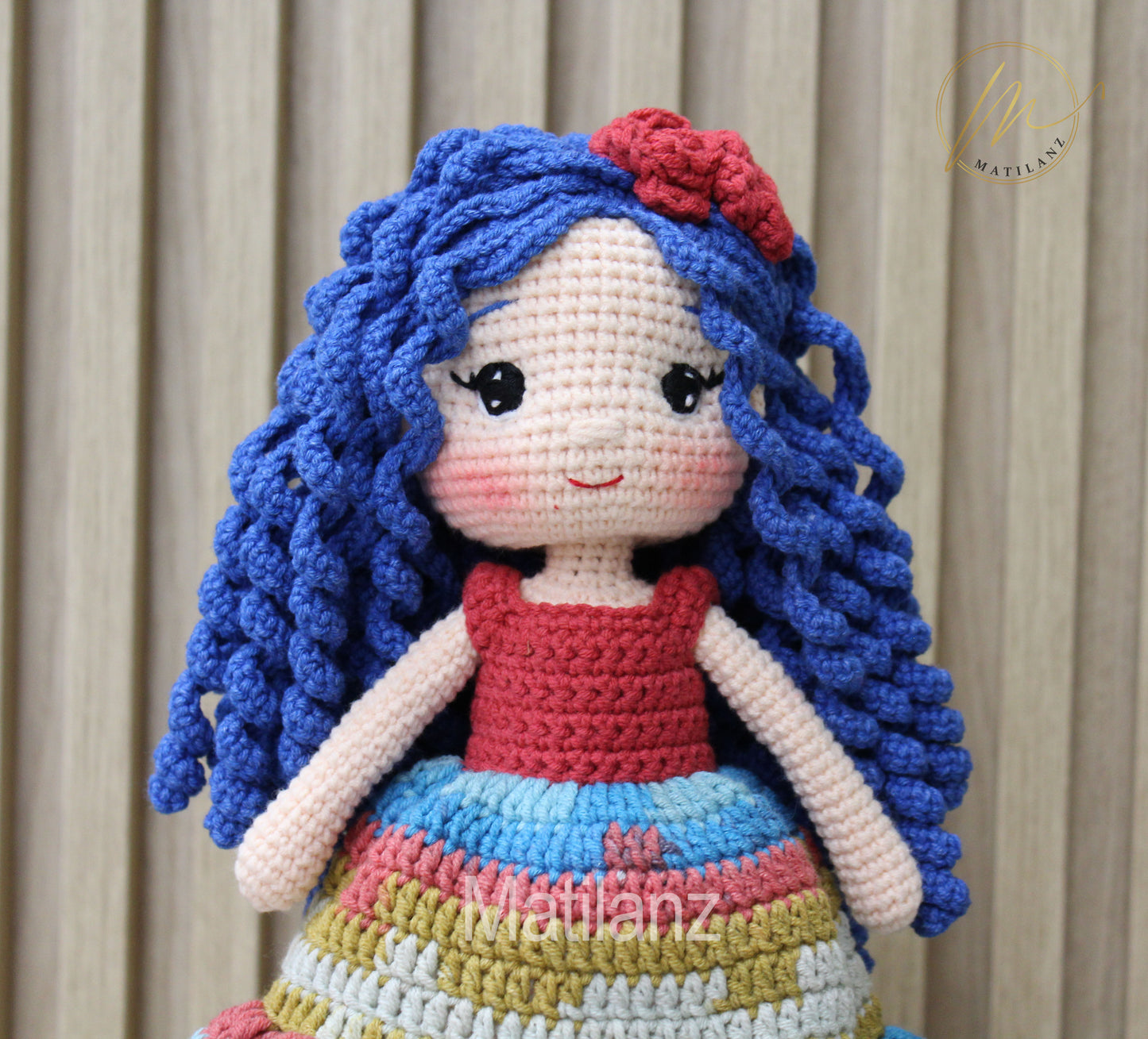 Hand-crocheted doll with blue curly hair and multicolored dress