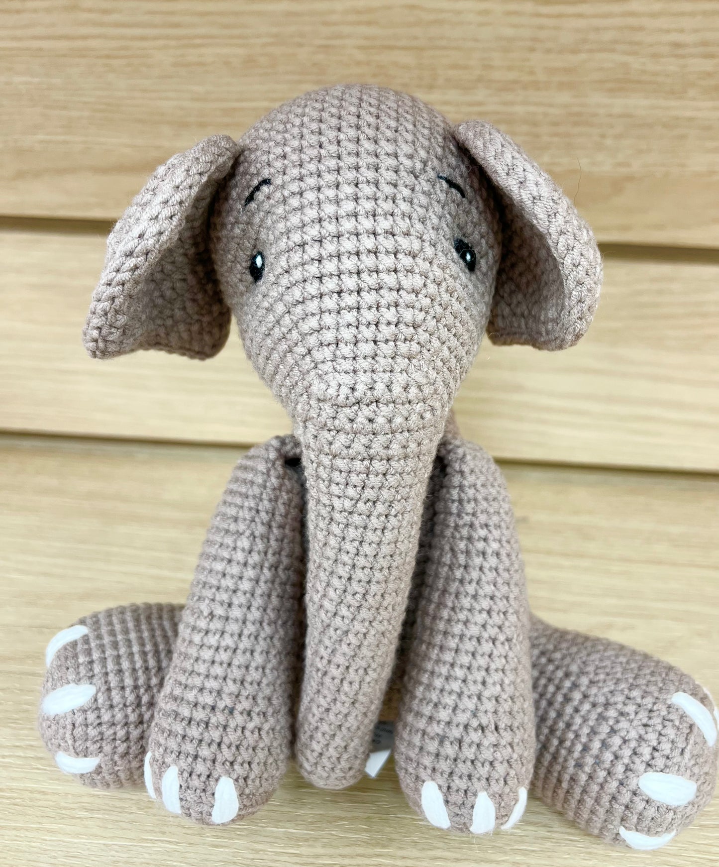 A handmade crochet elephant with large ears and embroidered eyes, sitting on a wooden surface.