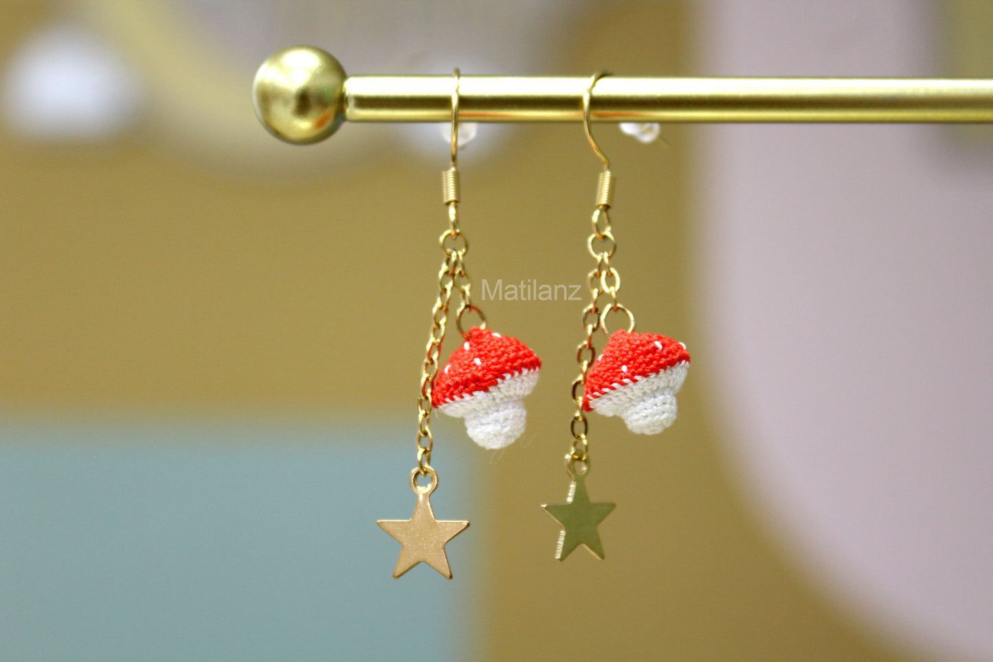 "Handmade crochet mushroom-shaped earrings with red tops, white stems, and gold star pendants."