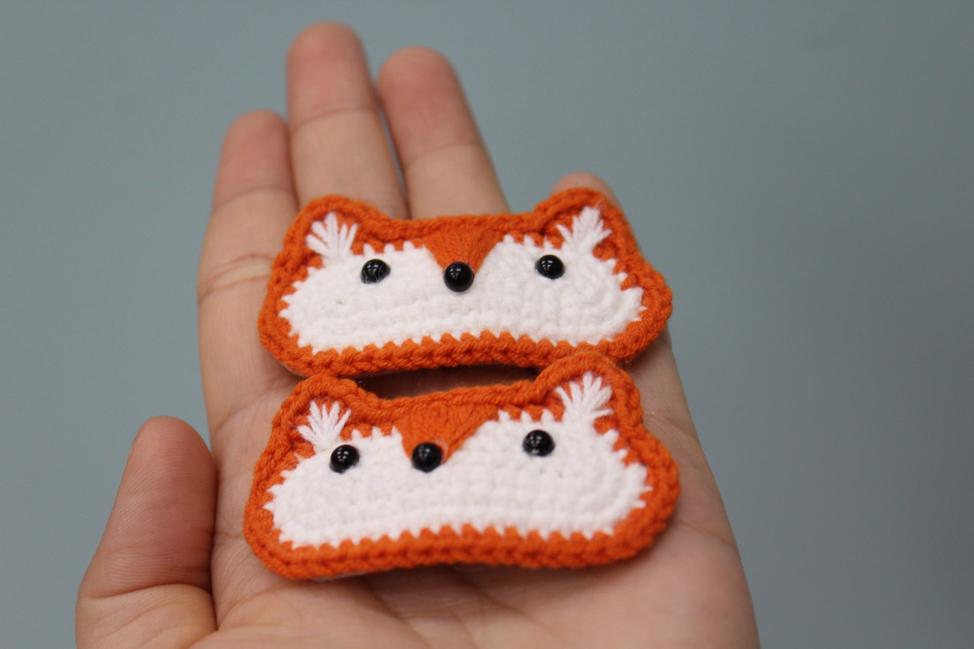 Two crochet fox hair clips, handmade in orange and white with cute, cartoon-style features.