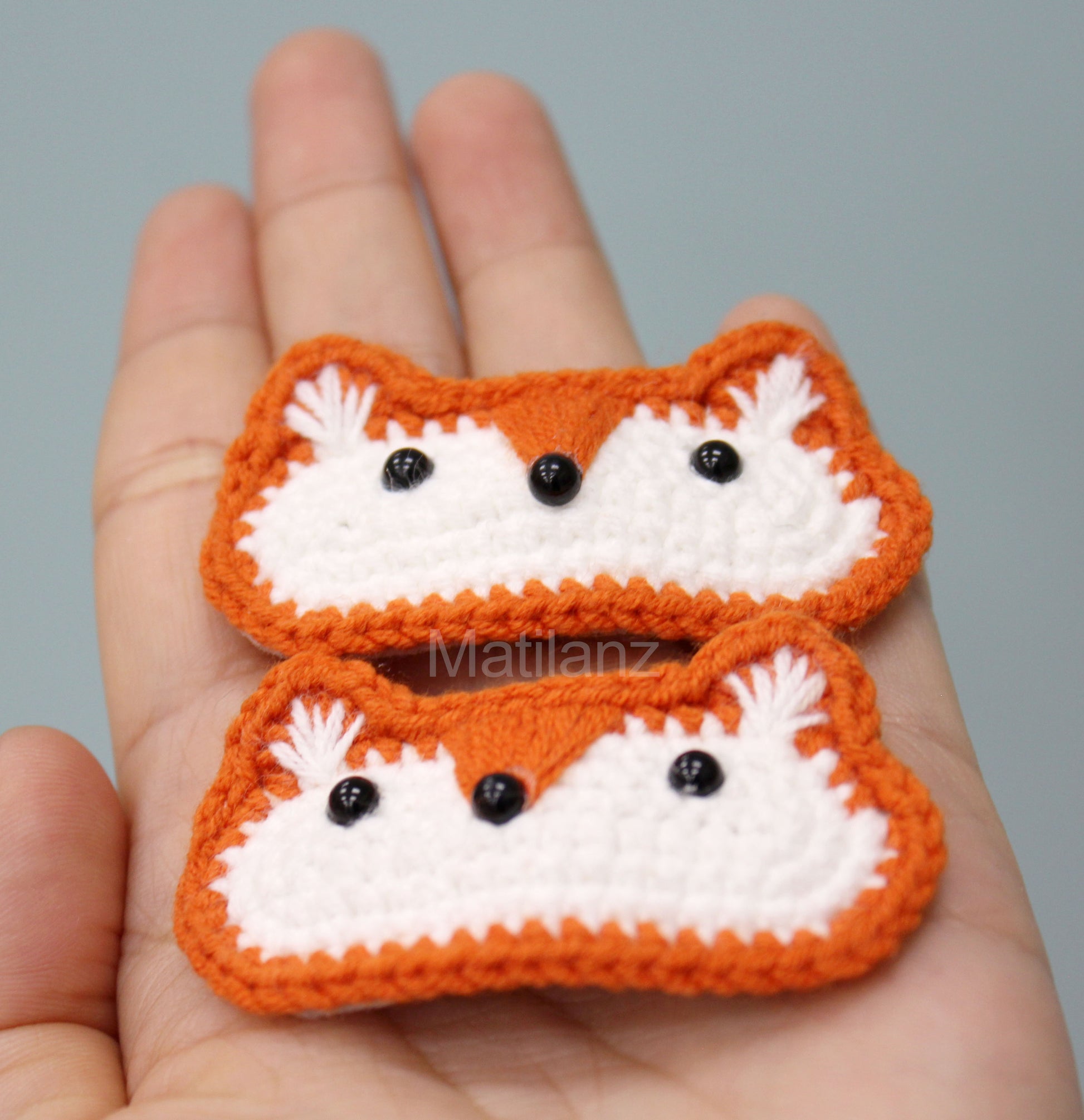 Crochet fox hair clips with orange and white yarn, featuring black bead eyes and fluffy white ears.