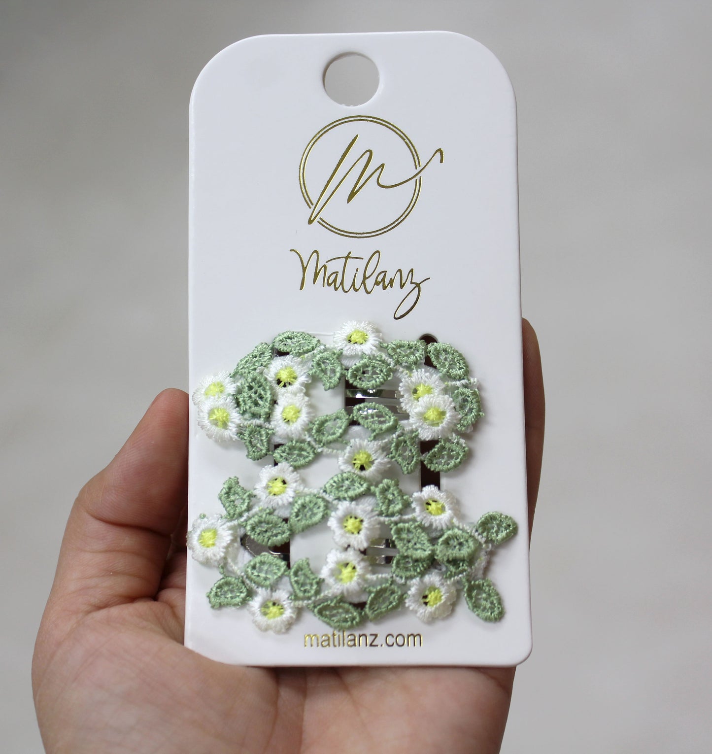 Charming floral embroidery hair clips with white daisies and green leaves, perfect for styling.