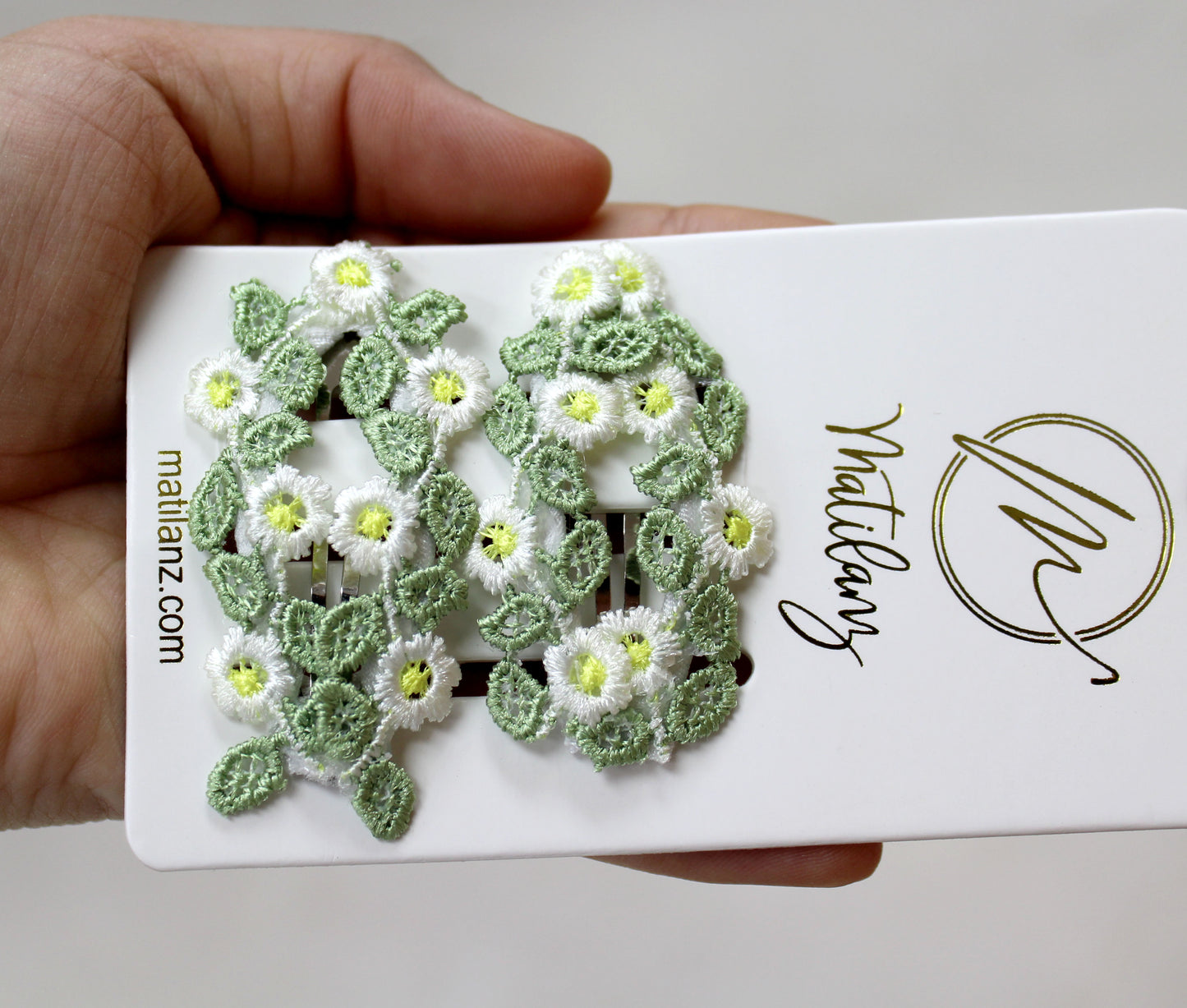 Charming floral embroidery hair clips with white daisies and green leaves, perfect for styling.
