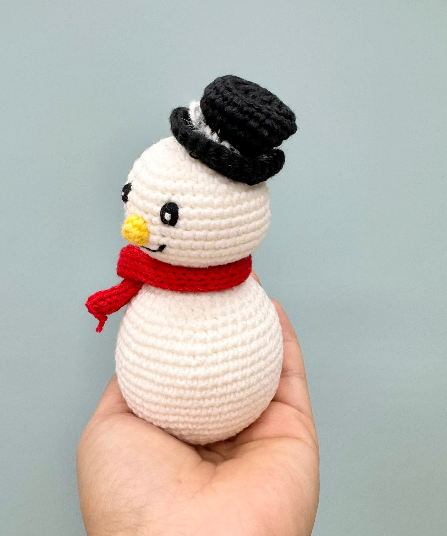 Crochet Christmas snowman with a black top hat, red scarf, and cheerful yellow nose.