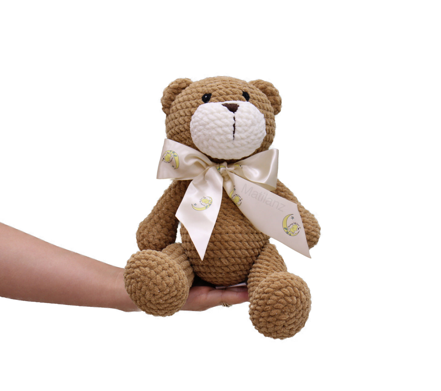 Handmade crochet teddy bear in brown plush with a white bow featuring a cute design.