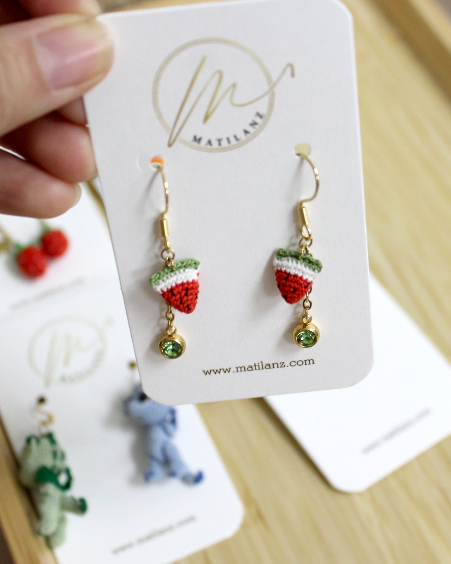 Handmade crochet strawberry earrings with green beads on gold hooks.