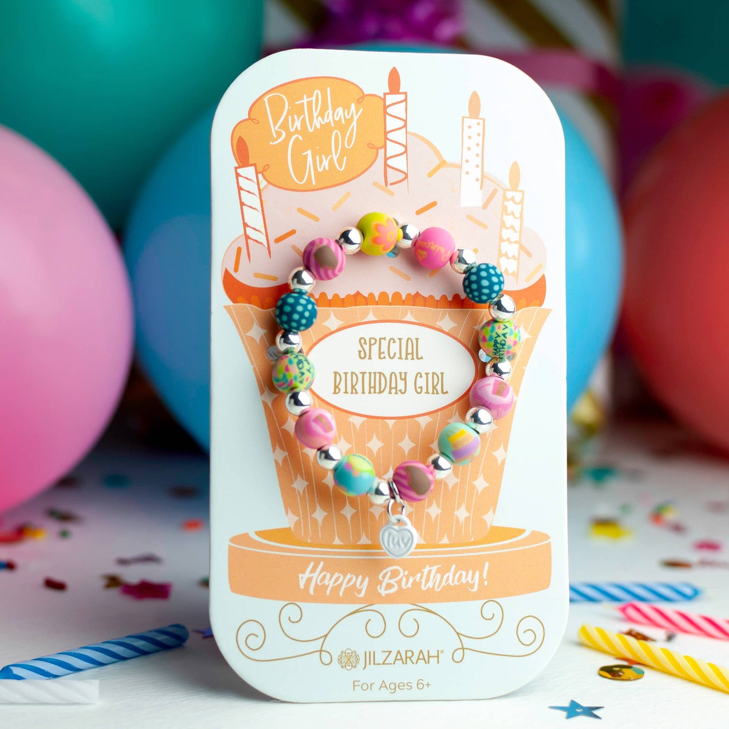 Youth birthday bracelet with vibrant polymer clay beads displayed on a cupcake-themed card among birthday decorations.