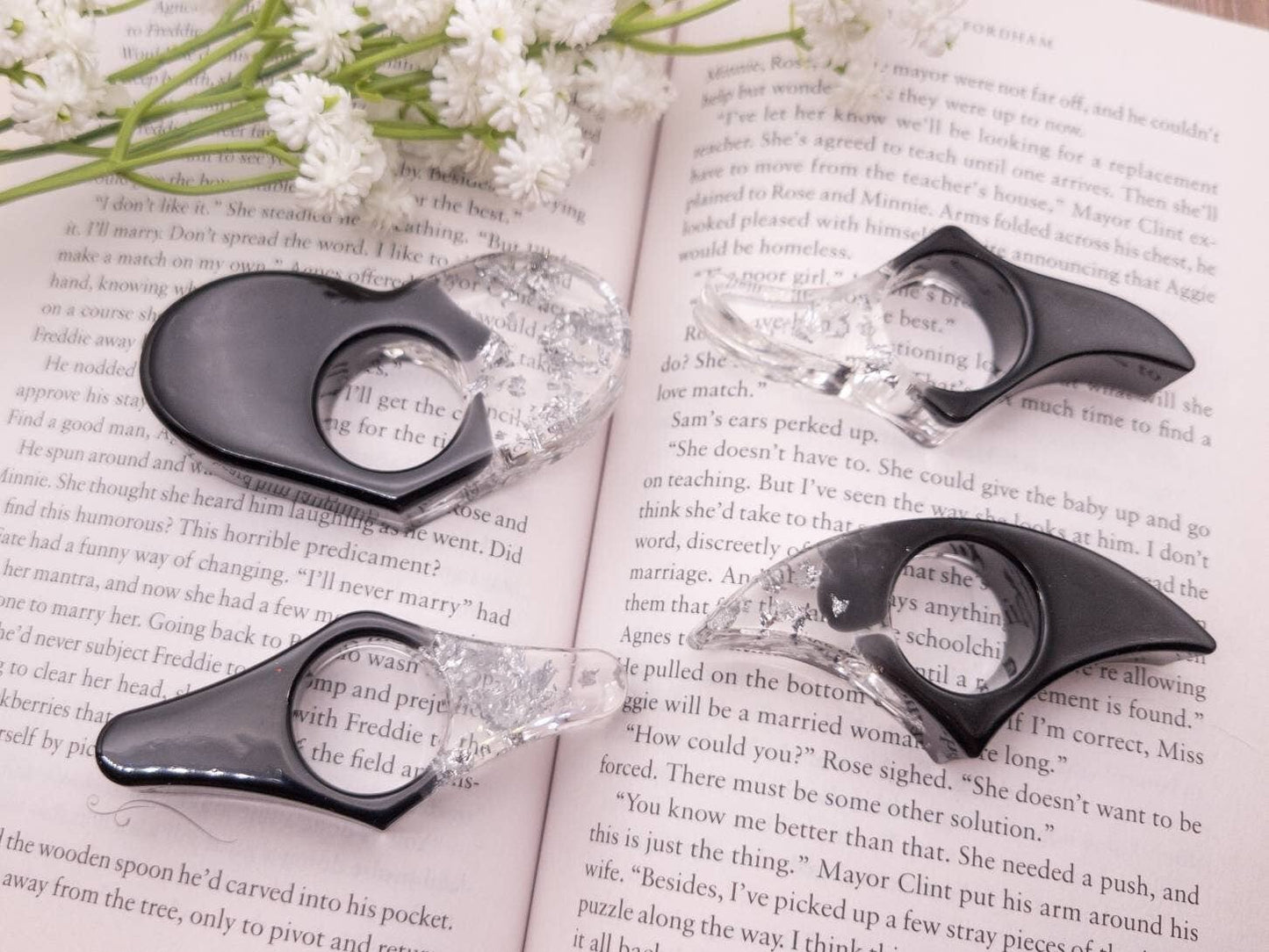 Black and silver book page holders resting on an open book surrounded by white flowers