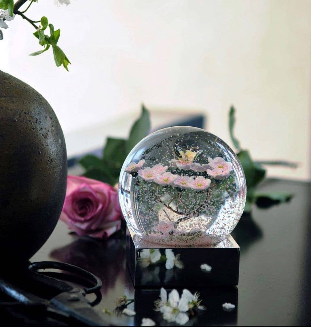 A clear glass snow globe featuring a delicate butterfly perched on a cherry blossom branch.