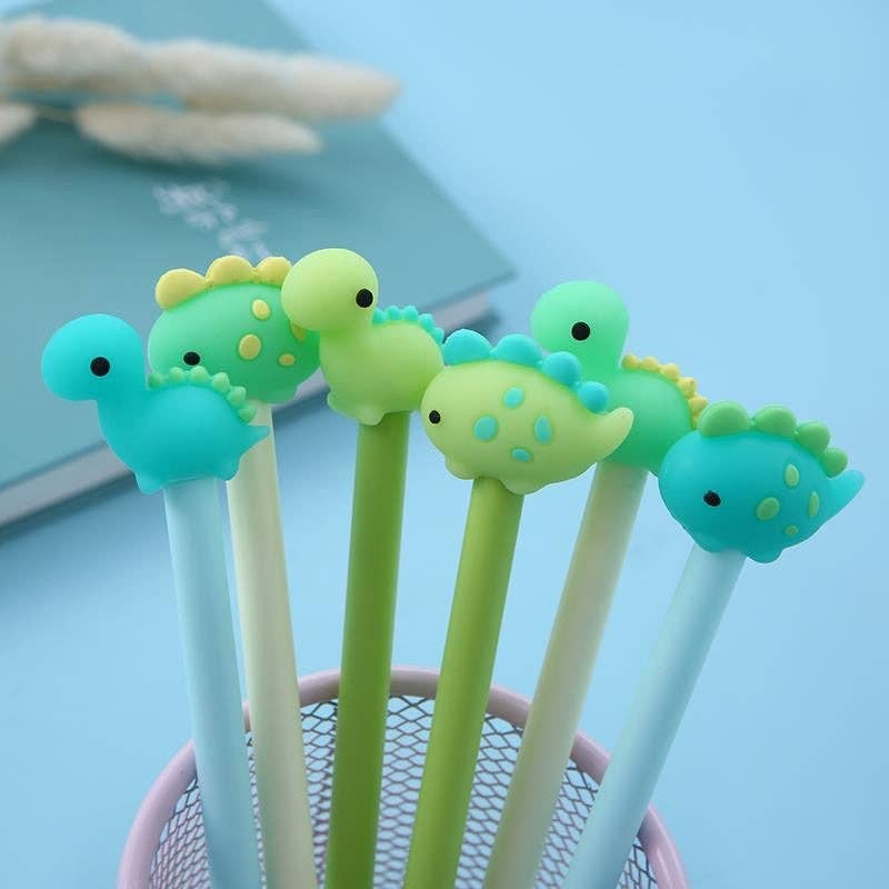 Assorted gel pens with soft rubber dinosaur toppers in shades of green, blue, and turquoise in a pencil holder on a blue background.