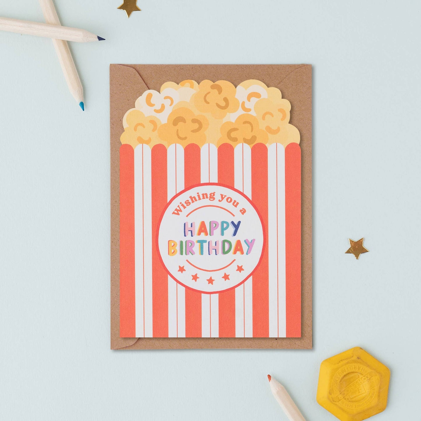 A quirky birthday card shaped like a red and white striped popcorn box with colorful "Happy Birthday" text.