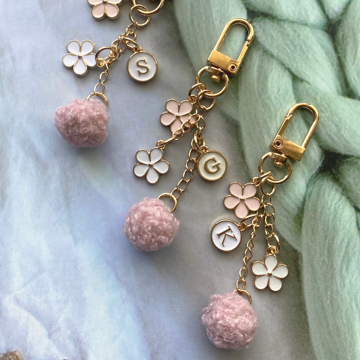 Charming keychain with gold chain, floral charms, initial disc, and fluffy pink pom charm.
