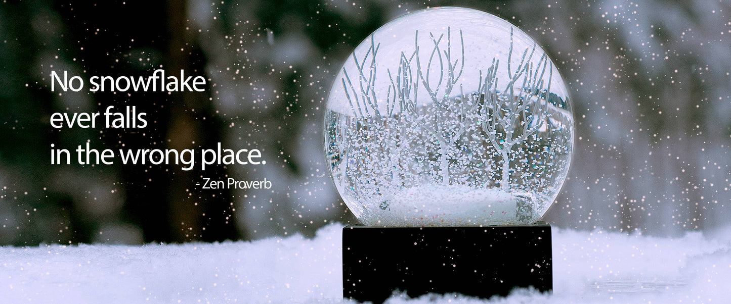 Winter snow globe with bare trees inside, set on a square black base.
